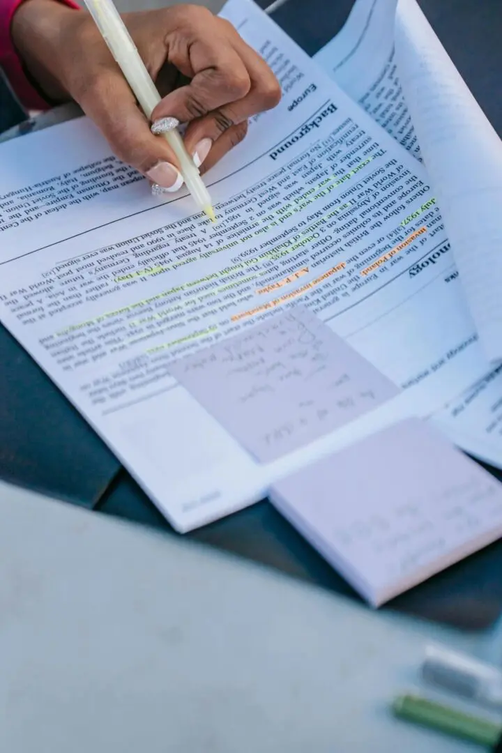 A person writing on top of papers with sticky notes.